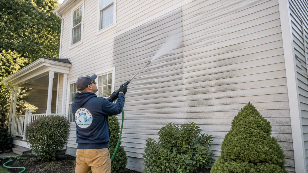 Homeowner using a pressure washer on house siding to understand why you should pressure wash your house annually